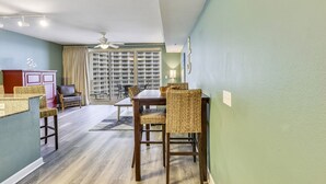 Comedor con mesa de madera y sillas de mimbre, ventilador de techo y vistas a través de un amplio ventanal.