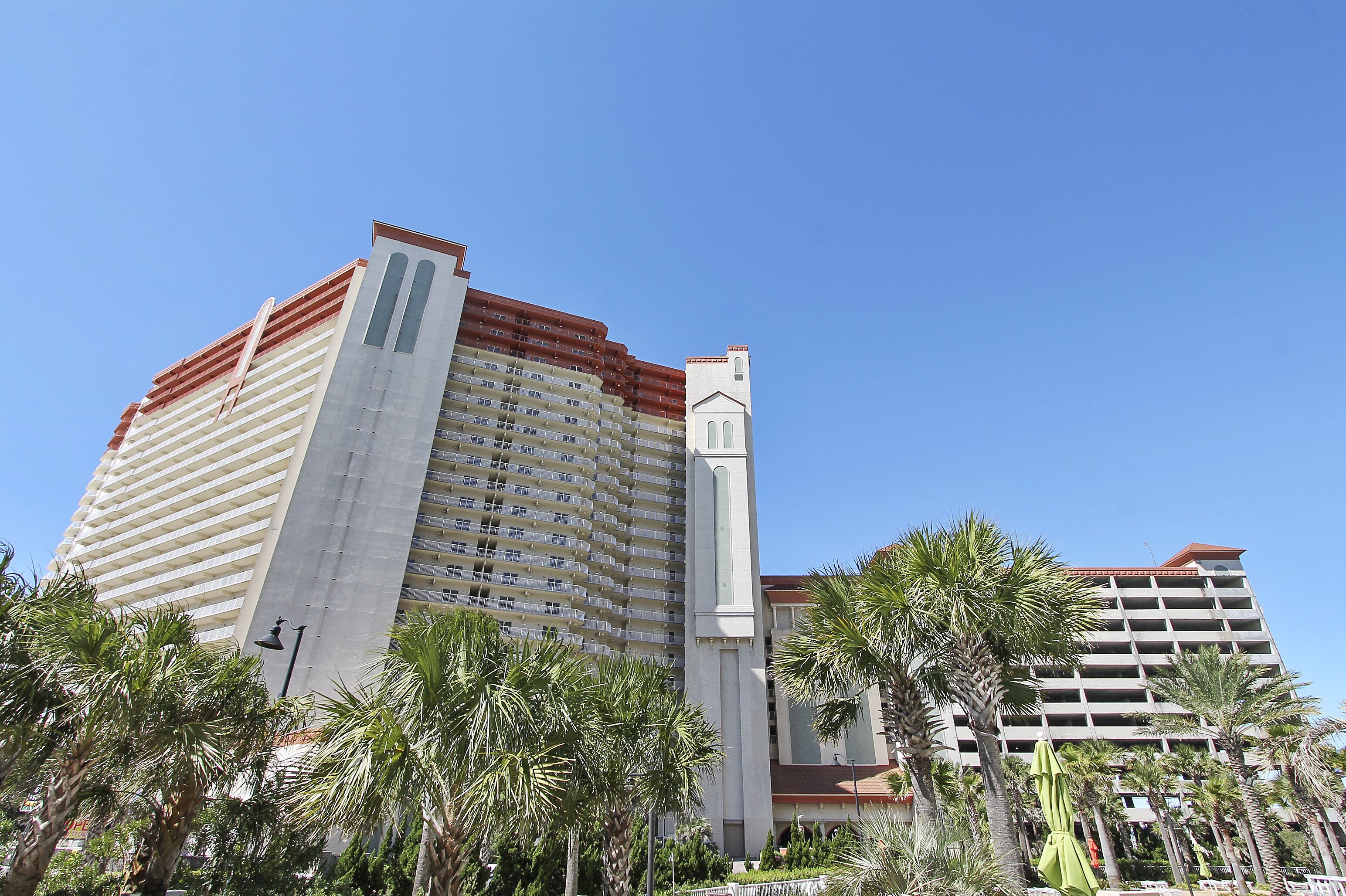 A multi-story hotel with a prominent corner structure, surrounded by palm trees.