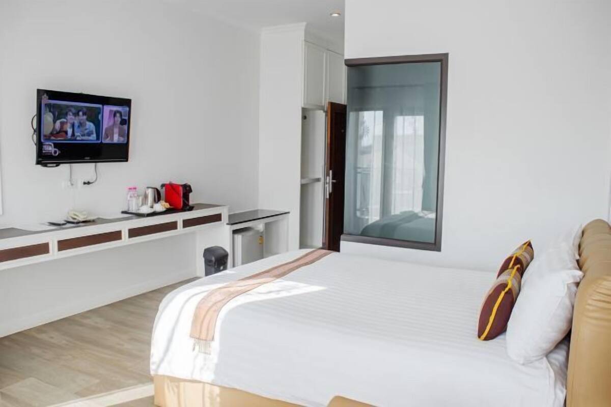 Een moderne hotelkamer met een groot bed, een aan de muur bevestigde televisie, een bureau met stoel en een raam met uitzicht.