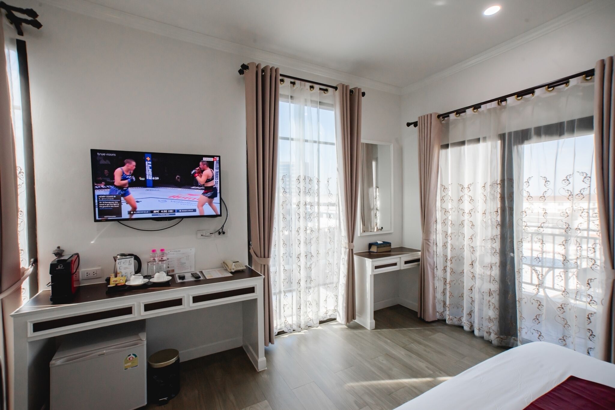 Une chambre d’hôtel équipée d’un téléviseur fixé au mur, d’un bureau avec un ordinateur, d’un petit réfrigérateur, d’une table de chevet et d’un lit.