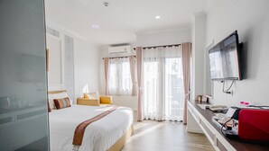 Een hotelkamer met een bed, een televisie, een bureau met telefoon en een raam met gordijnen.
