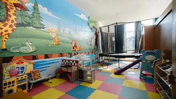 Une salle de jeux pour enfants avec un sol coloré, une fresque représentant des animaux, des structures de jeu et une fenêtre donnant sur un paysage.