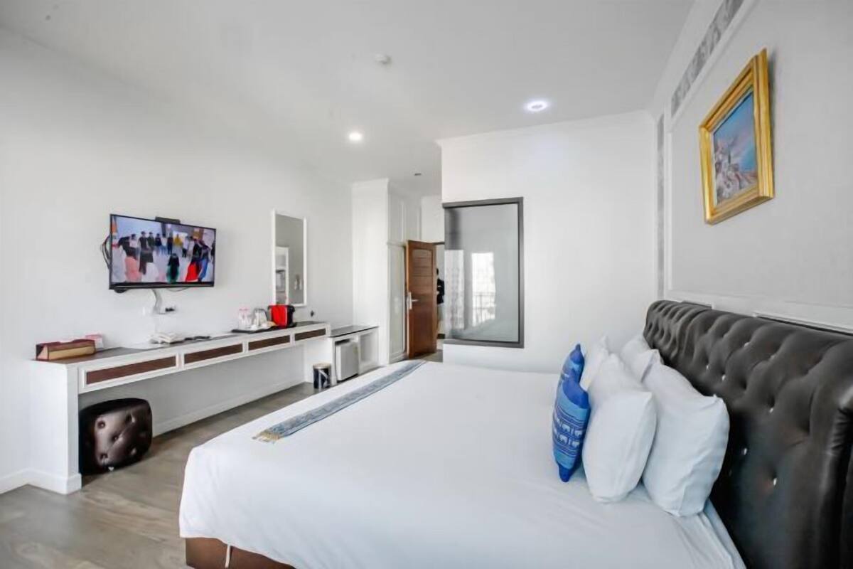 Habitació d'hotel moderna amb un llit gran, una televisió de pantalla plana, un escriptori amb un ordinador i un mirall.