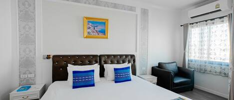 Habitación de hotel con una cama grande, cabecero, mesita de noche, una silla, ventana con cortinas y un cuadro en la pared.