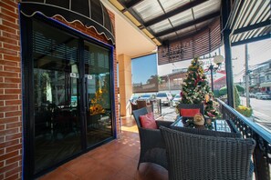 Un restaurant doté d’une façade en verre, d’une terrasse avec des meubles en osier et d’un sapin de Noël.