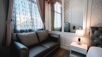 Ein Zimmer mit einem dunklen Ledersofa, einem Nachttisch mit Lampe und einem Fenster mit gemusterten Vorhängen.