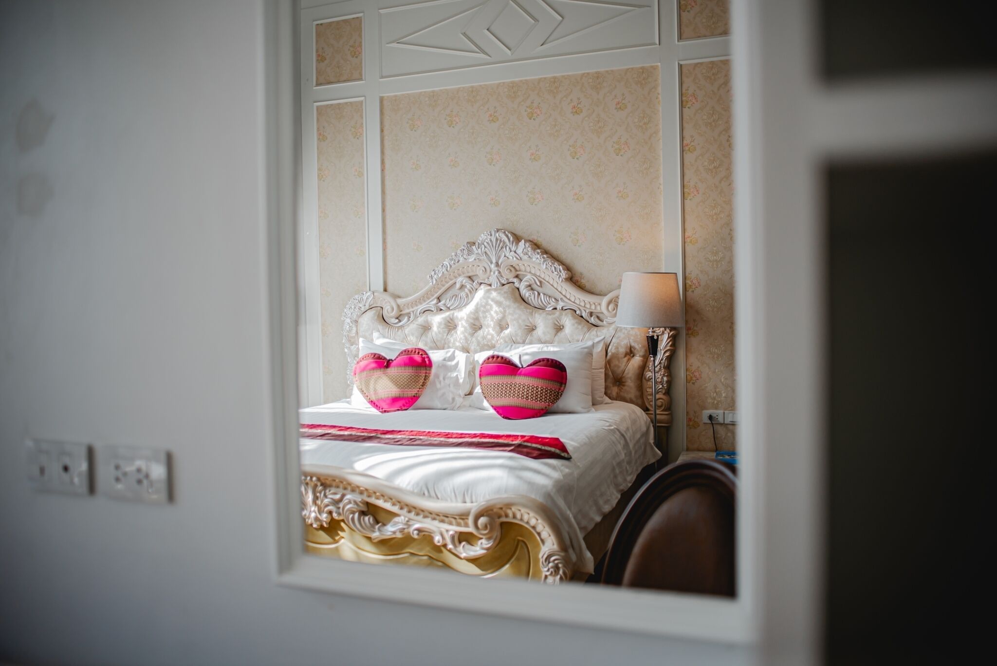 A bed with ornate headboard, white bedding, and two heart-shaped pillows.