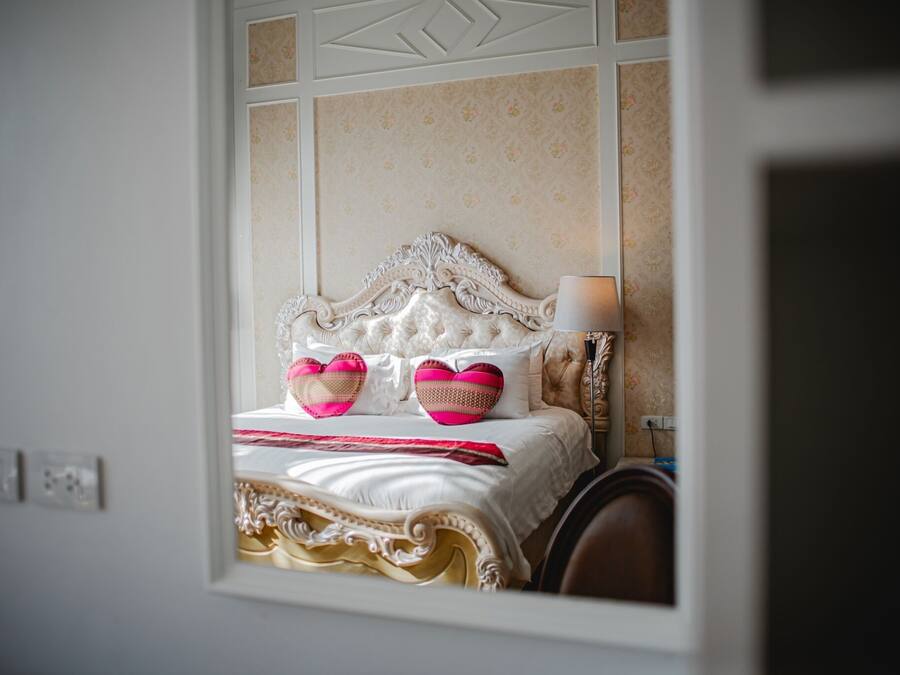 A bed with ornate headboard, white bedding, and two heart-shaped pillows.