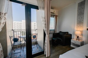 Une chambre d’hôtel avec un balcon, un lit, une table de chevet avec une lampe et un fauteuil en cuir noir.