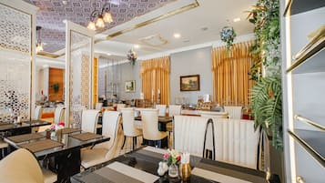 Un restaurante con una decoración moderna, que presenta un techo con diseños, paredes blancas y una zona de bar con una planta decorativa.