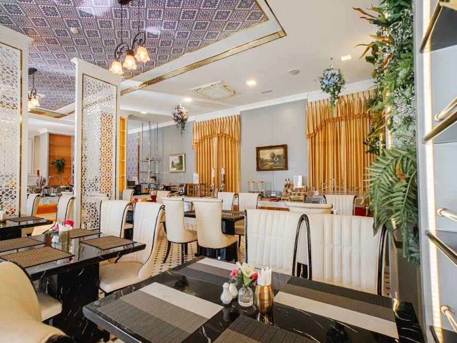 Un restaurante con una decoración moderna, que presenta un techo con diseños, paredes blancas y una zona de bar con una planta decorativa.