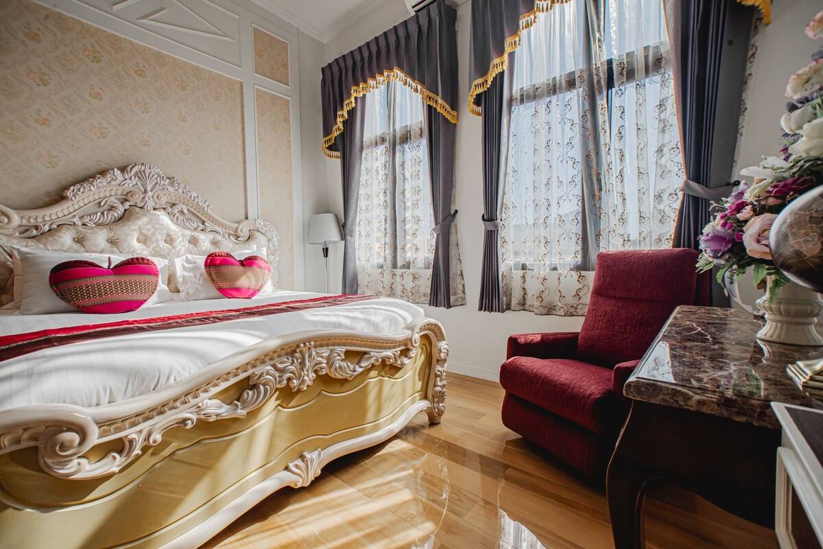 Een luxueuze slaapkamer met een sierlijk bed, een rode fauteuil en een marmeren tafel.