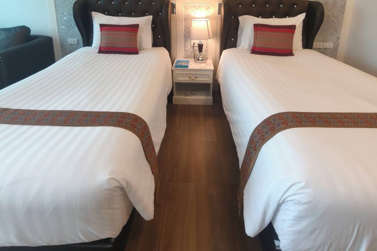 Een hotelkamer met twee bedden, een nachtkastje met een lamp en een ingelijst foto aan de muur.