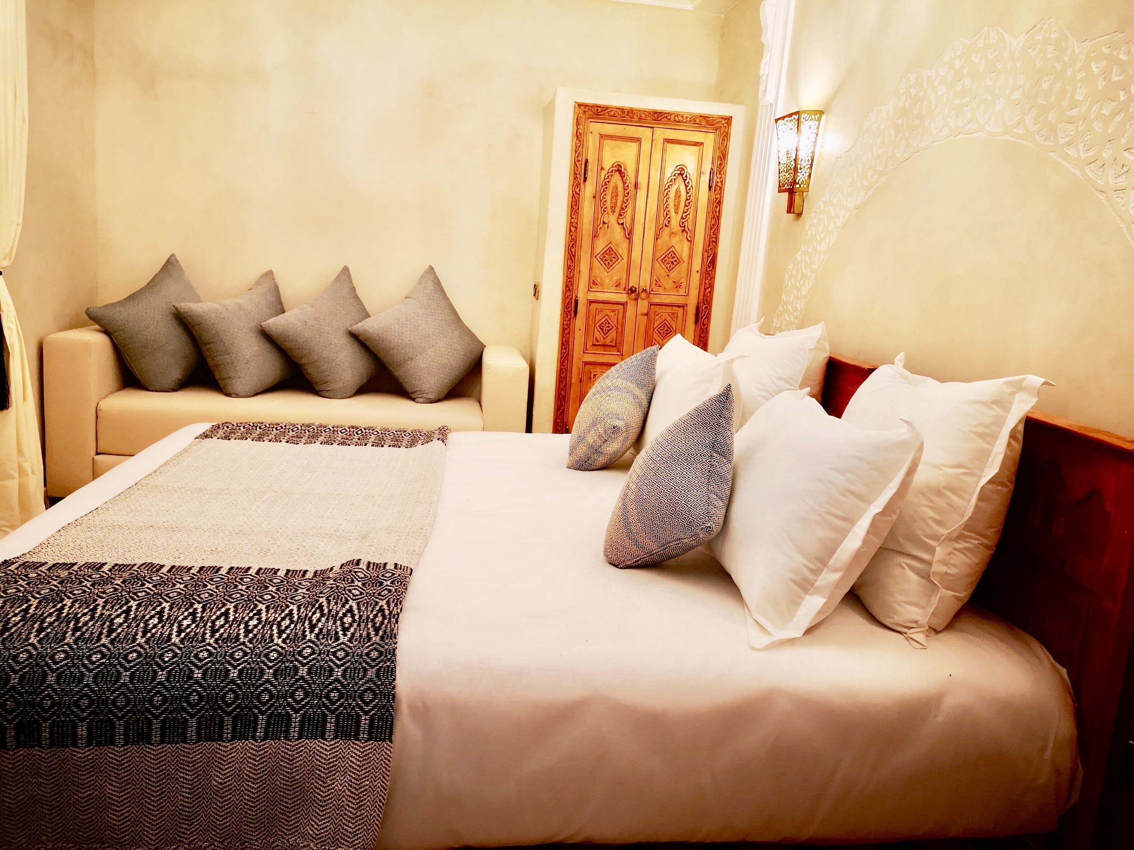 A neatly arranged bedroom with a bed, pillows, a sofa, and a door.