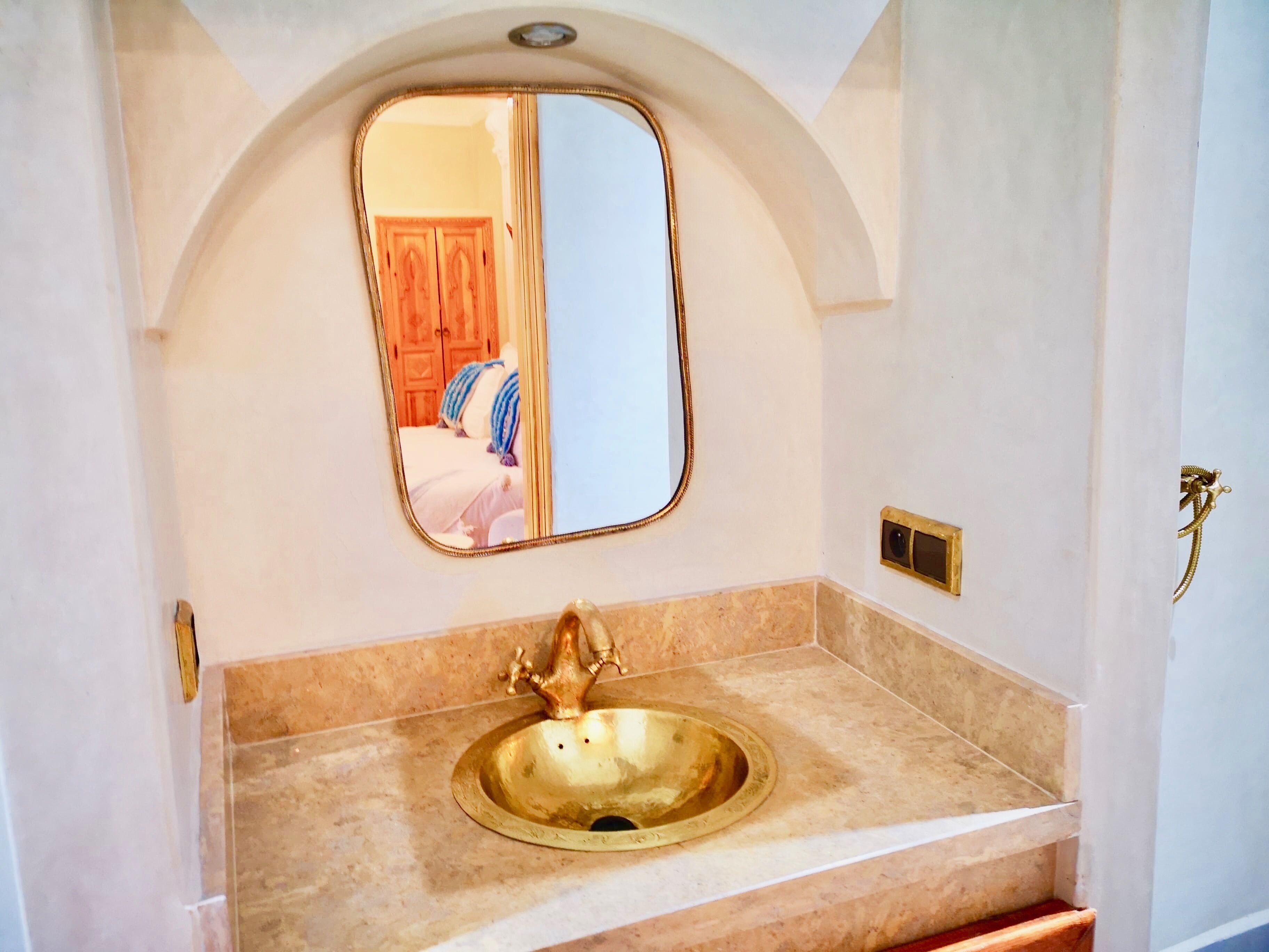A bathroom with a gold sink, a mirror, and a wooden door in the background.