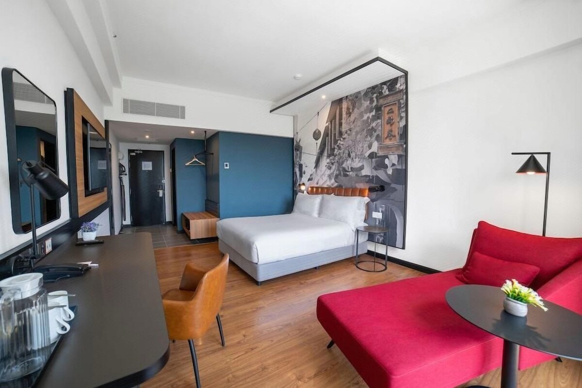 A hotel room with a bed, a red sofa, a dining table, and a wall with a mural.