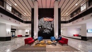Un vestíbulo amplio con una gran pared de bienvenida que muestra saludos en varios idiomas, dos sofás rojos y una decoración de diseño moderno.