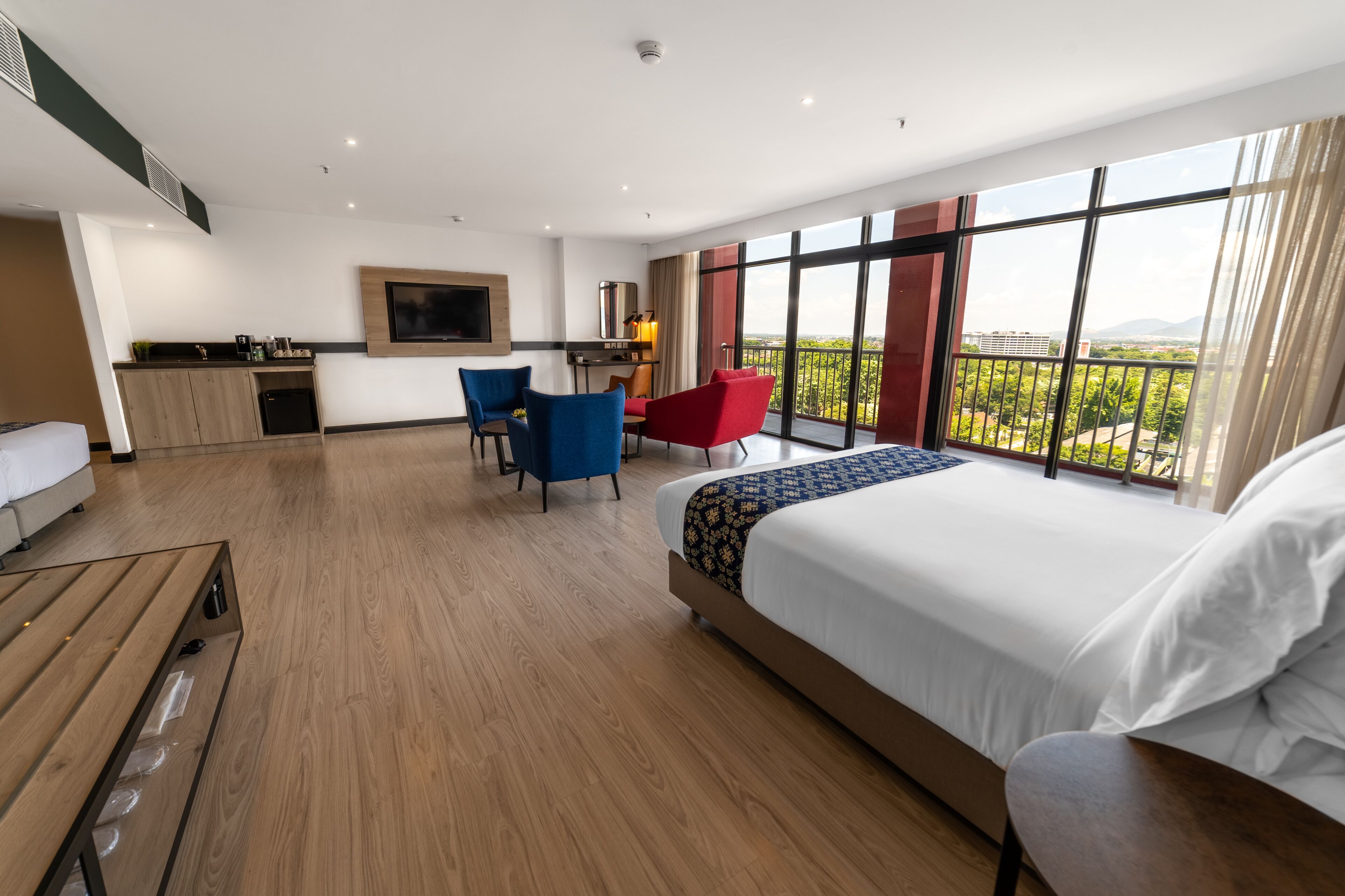 A modern hotel room with a large bed, a desk, a chair, and a balcony with a view.