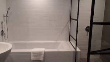 Un baño con una bañera blanca, un lavamanos blanco y una cabina de ducha con mampara de vidrio.