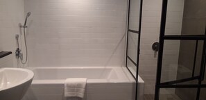 A bathroom with a white bathtub, a white sink, and a glass shower enclosure.