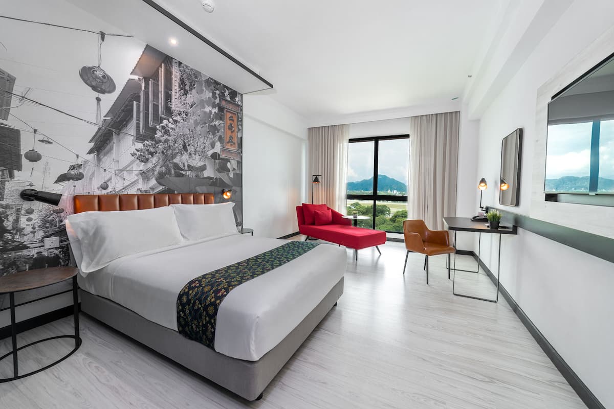 A modern hotel room with a large bed, a red chair, a desk, and a cityscape view.