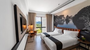 Habitación de hotel con dos camas, un escritorio, una silla y un ventanal con vistas a un lago y montañas.