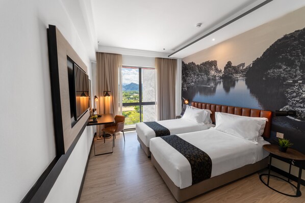 A hotel room with two beds, a desk, a chair, and a large window with a view of a lake and mountains.
