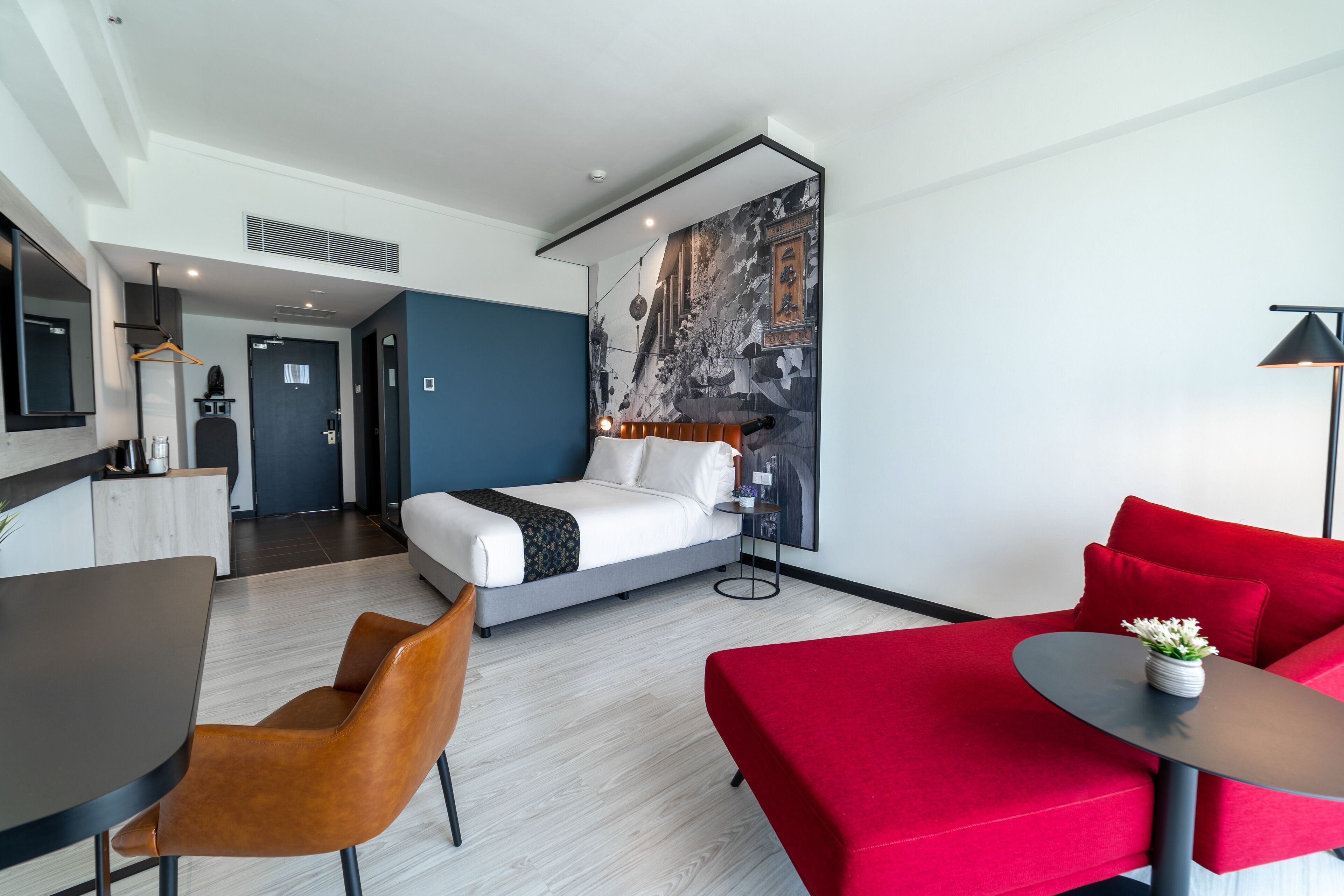 A modern hotel room with a bed, a red sofa, a small table, and a desk.
