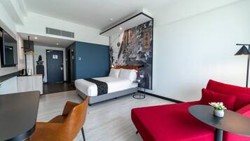 A modern hotel room with a bed, a red sofa, a small table, and a desk.