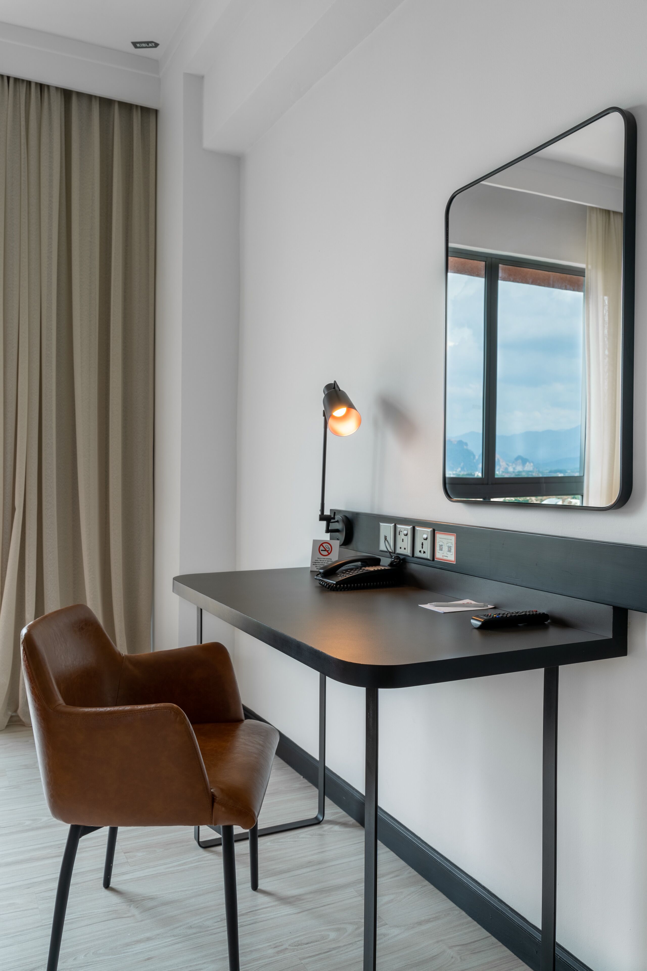 A modern hotel room with a desk, a chair, a lamp, a telephone, and a window with a view.