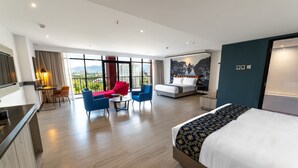 Una habitación de hotel moderna con una cama grande, un área de comedor con mesa y sillas, y un balcón con vistas a la ciudad.