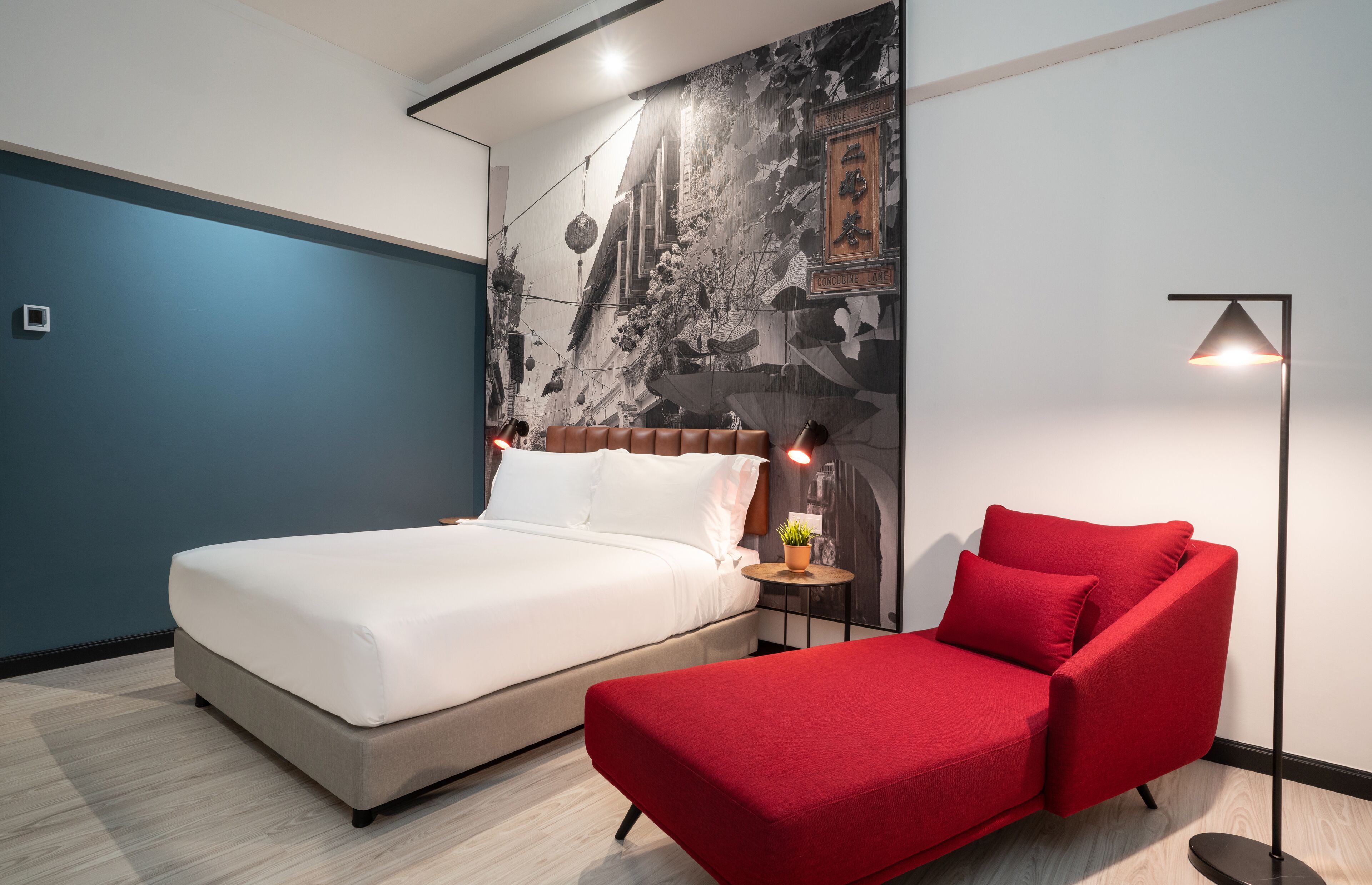Un dormitorio moderno con cama, sofá rojo, mesita de noche y un mural en la pared.