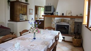 Un coin repas chaleureux avec une table dressée pour deux personnes, une cheminée et un téléviseur en arrière-plan.