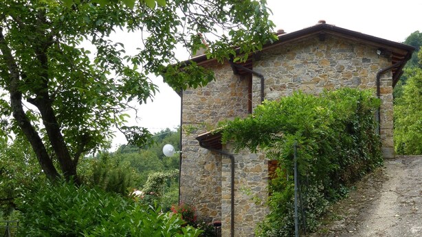Un bâtiment en pierre doté d’un toit en pente, entouré d’une végétation luxuriante et accessible par un chemin de gravier menant à l’entrée.