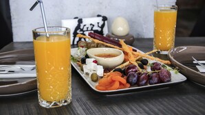 Una mesa con un plato de bocadillos, dos vasos de zumo de naranja y un objeto decorativo al fondo.