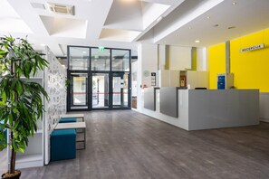 A reception area with a glass door entrance, a reception desk, and a seating area with blue cushions. - Rooms Dr. Franjo Tuđman - Hostel (Split)