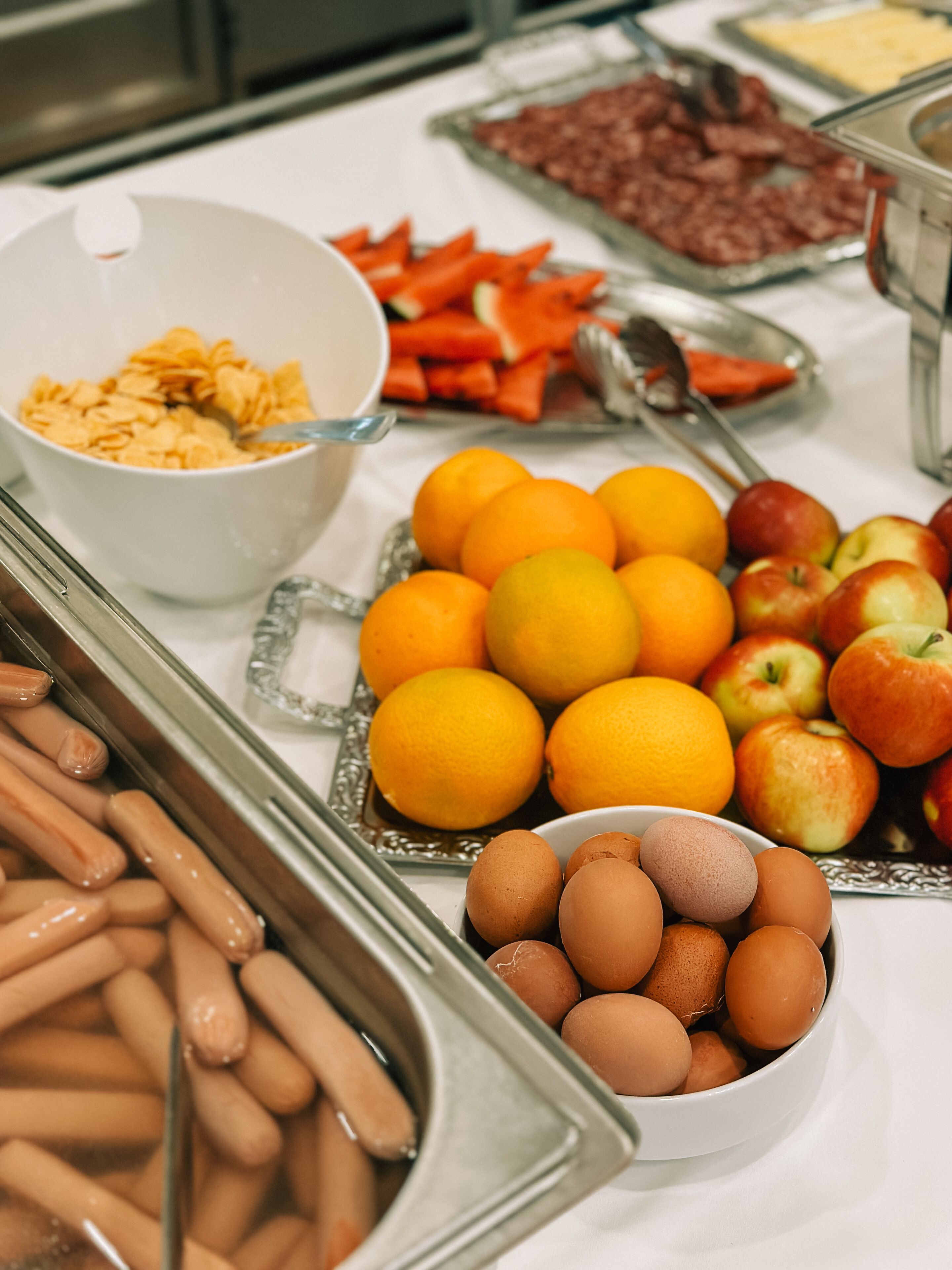 Buffet com diversos alimentos, incluindo frutas, ovos e salsichas.