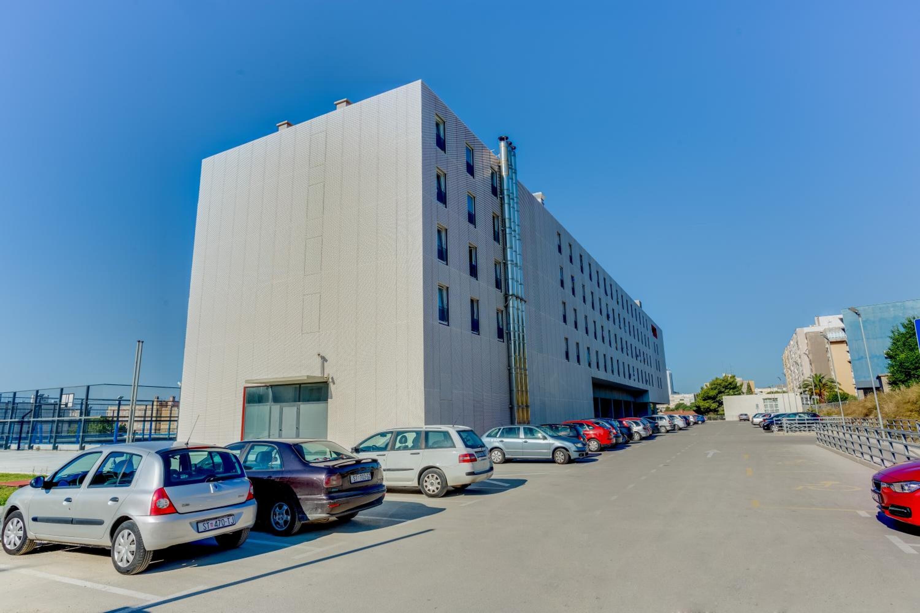 A parking lot with several cars parked in front of a modern building with a large garage door.