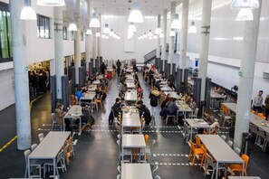 A spacious cafeteria with multiple tables and chairs, high ceilings, and pendant lighting. - Rooms Dr. Franjo Tuđman - Hostel (Split)