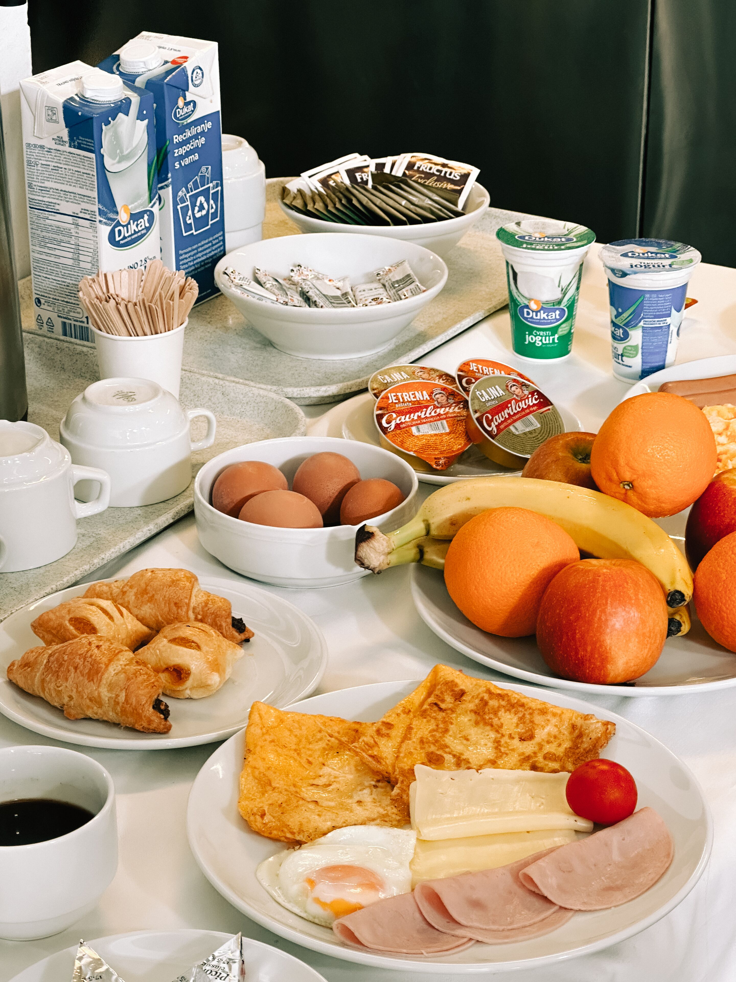 Una tavola imbandita per la colazione, con uova, frutta, pasticcini e latticini.