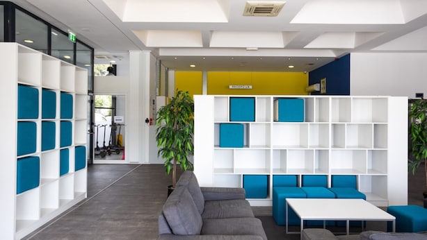 Ein moderner Empfangsbereich mit grauem Sofa, blauen Kissen und weißen Regalelementen.