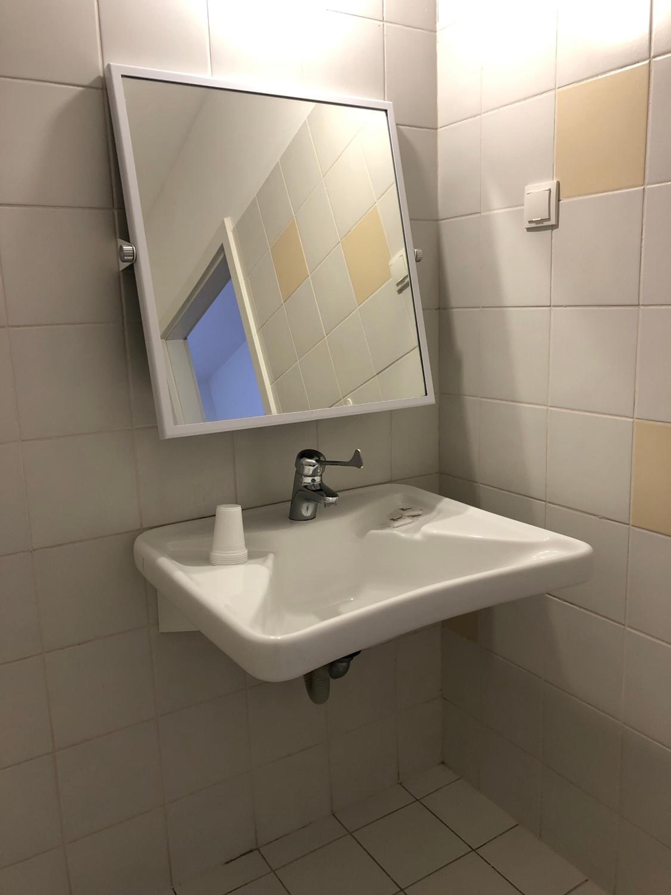 Een badkamer met een wit wastafel, een spiegel en een waterkraan.