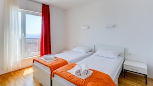 Ein Hotelzimmer mit zwei Betten, einem Fenster mit Vorhängen, Holzboden und einem kleinen Nachttisch.