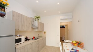 A compact kitchen with a microwave, stove, and cabinets. There's a dining table with chairs and a bowl of fruit.