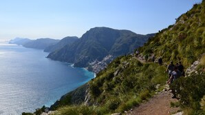 A coastal hiking trail with a clear view of the sea and distant mountains.