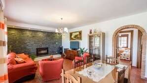 Un salon avec un mur en pierre, des canapés rouges, une cheminée et un coin repas comprenant une table et des chaises.