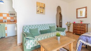 A cozy living room with a sofa, a wooden coffee table, and a kitchen area with a microwave and a refrigerator. - Estudio Juzcar Júzcar by Ruralidays (Málaga)