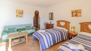 A room with two beds, a sofa, a wooden table, and a mirror. - Estudio Juzcar Júzcar by Ruralidays (Málaga)