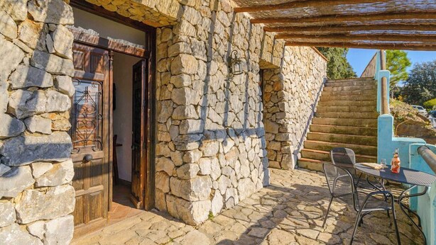 A stone building with a wooden door, a staircase, and outdoor seating. - Estudio Juzcar Júzcar by Ruralidays (Málaga)