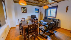 A dining area with a wooden table and chairs, a sofa, and a television. - Casa Genal Júzcar by Ruralidays (Málaga)